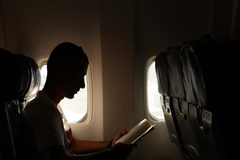 A man reading a book by the window, captured in a silhouette during flight.